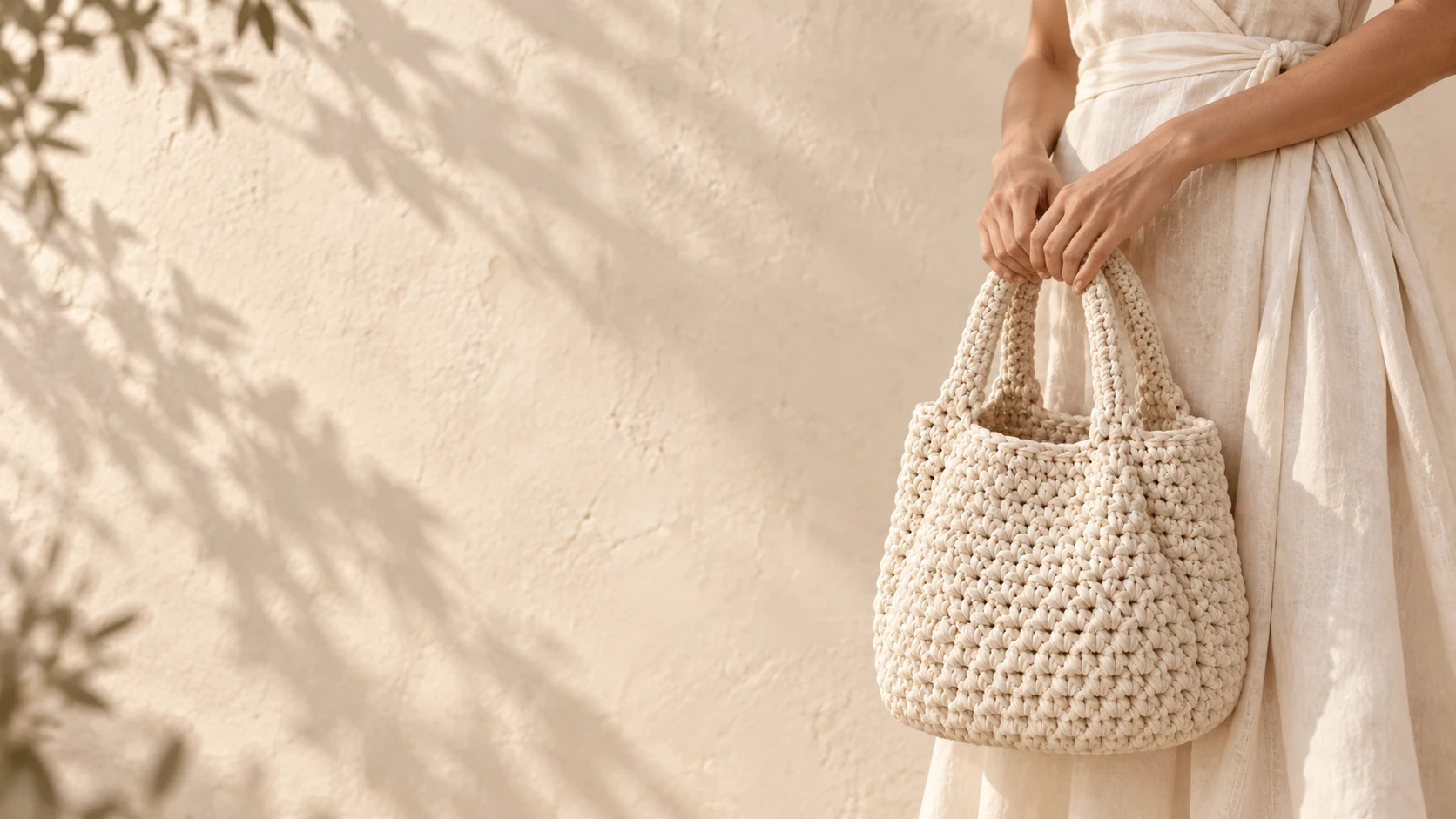Imagem editorial de uma bolsa de crochê areia, carregada à mão com um vestido de linho claro